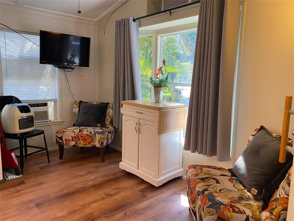 A room features two patterned armchairs, a white kitchen island, and a wall-mounted television — 1300 N RIVER ROAD UNIT W 86, VENICE, FL
