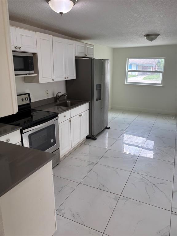 A kitchen with white cabinets, stainless steel appliances, gray countertops, and white marble-patterned tile flooring — 519 KATHERINE AVENUE, ORLANDO, FL
