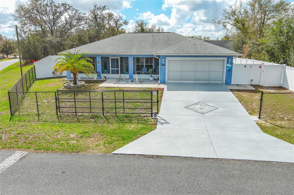A blue single-story house features a front porch, a two-car garage, and a fenced yard — 9430 SE 158TH STREET, SUMMERFIELD, FL