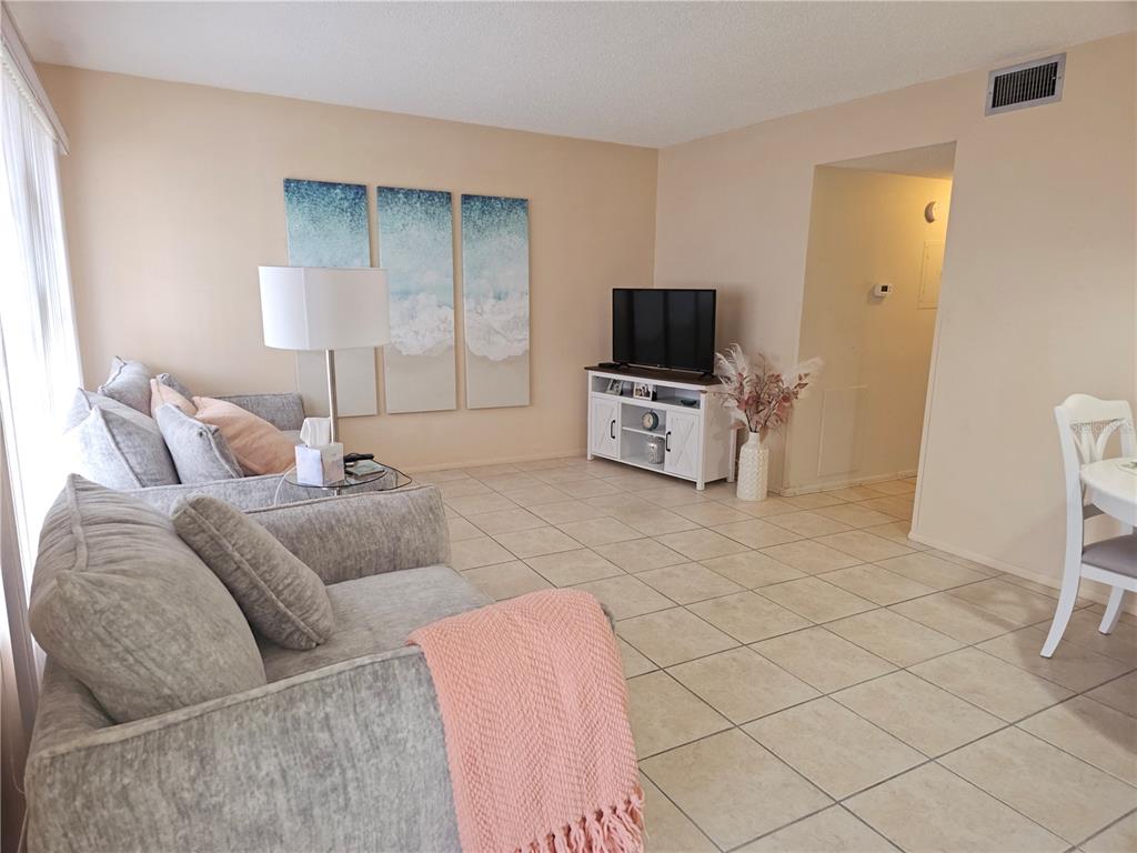 A living room features light tile flooring, gray sofas, a television stand, and wall art — 2458 COLUMBIA DRIVE UNIT 66, CLEARWATER, FL