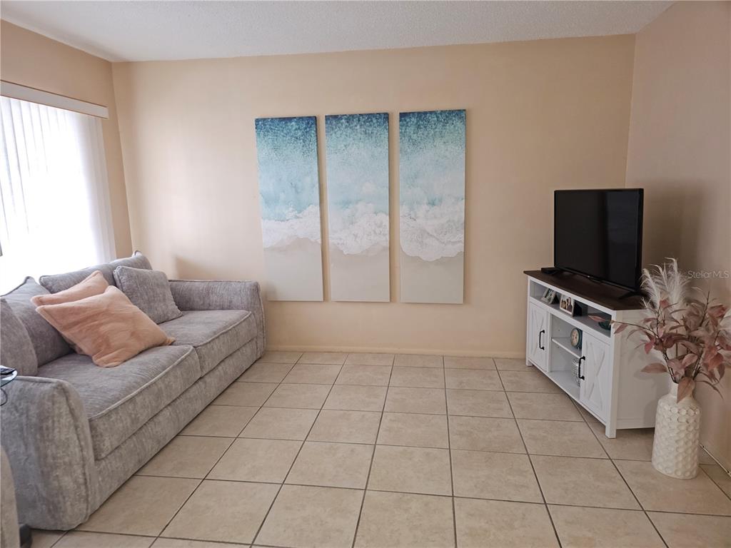 A living room features a grey sofa, a white media console, and three beach-themed wall canvases — 2458 COLUMBIA DRIVE UNIT 66, CLEARWATER, FL