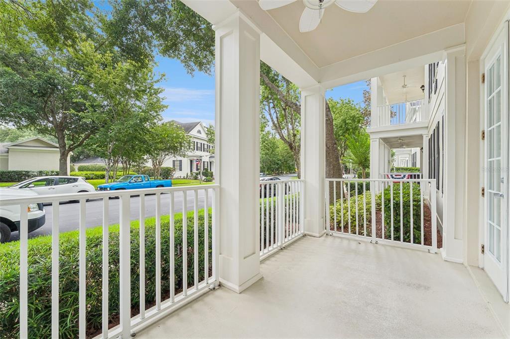A covered porch with white railings, columns, and a ceiling fan overlooks a street — 855 BLUE SAGE STREET UNIT 102, CELEBRATION, FL
