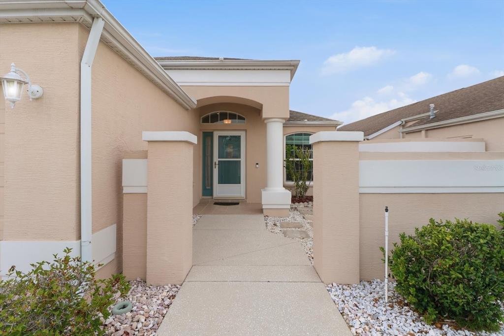 A concrete walkway leads to the front entrance of a beige stucco house — 250 ROYAL PALM WAY, SPRING HILL, FL