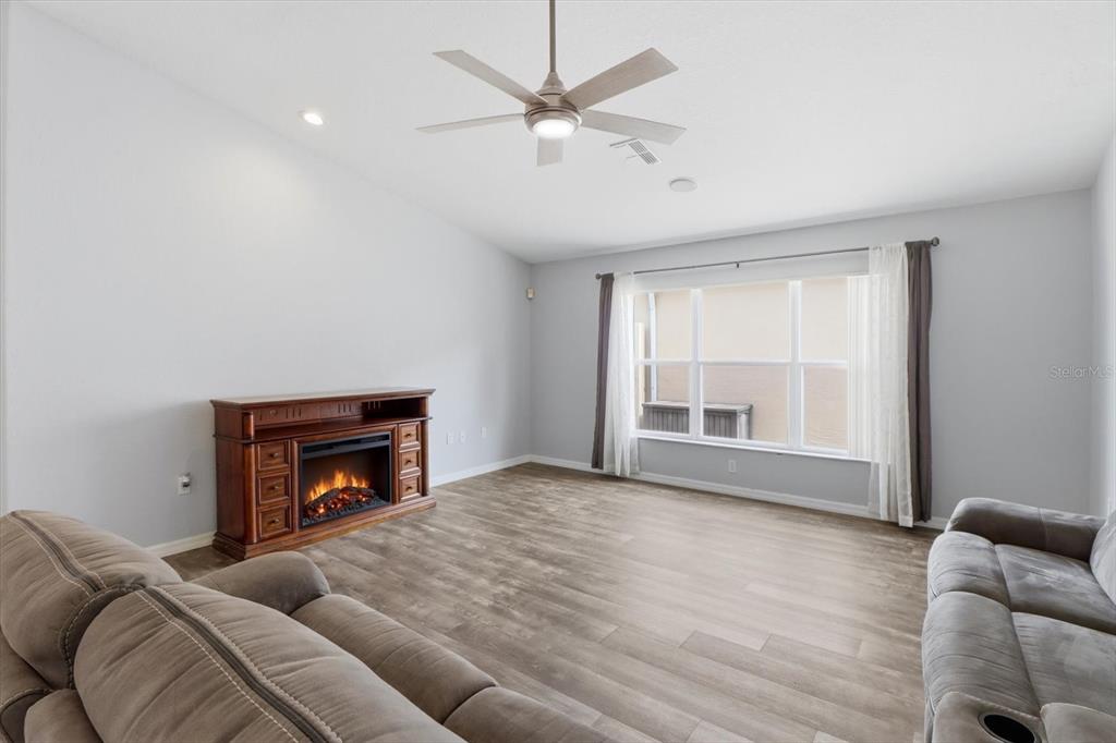 A living room features wood-look flooring, a ceiling fan, and an electric fireplace console — 250 ROYAL PALM WAY, SPRING HILL, FL