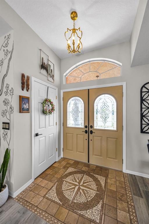 An entryway features a compass rose tile floor, double front doors, and a gold chandelier — 11210 AUBURNDALE STREET, SPRING HILL, FL