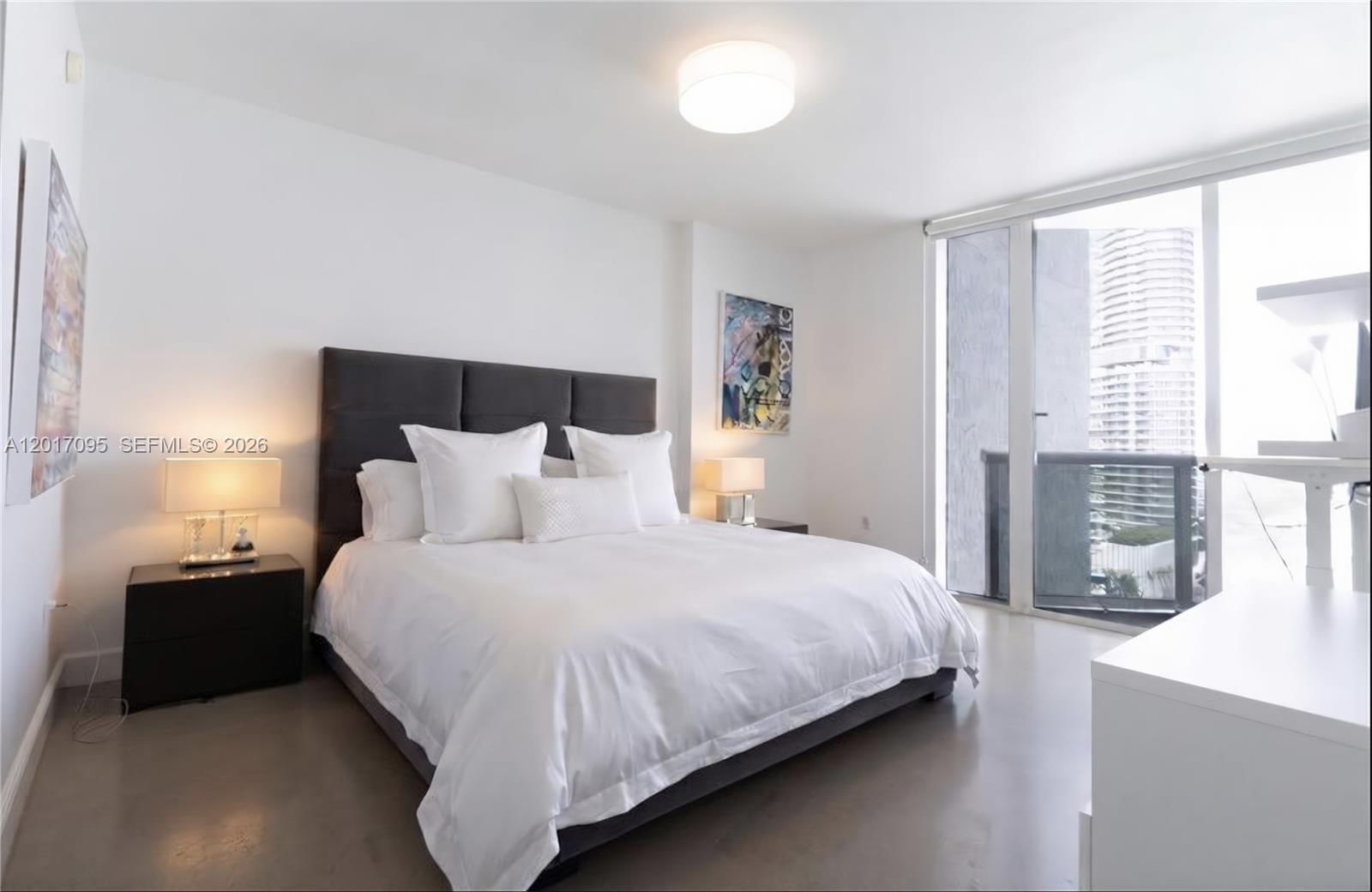 A modern bedroom features a dark upholstered bed, white bedding, and a balcony with city views — 400 Alton Rd # 1709, Miami Beach FL 33139, MIAMI BEACH, FL