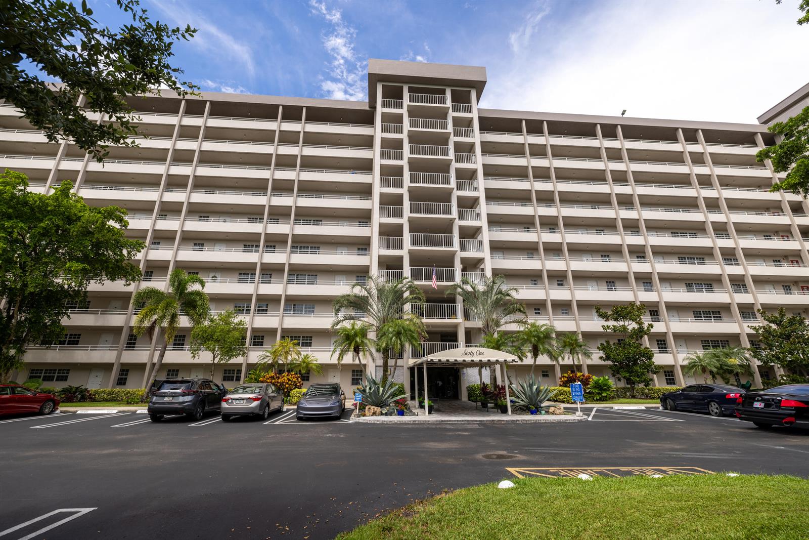 A multi-story apartment building features a central entrance canopy and a parking lot in front — 575 Oaks Lane # 708, Pompano Beach FL 33069, POMPANO BEACH, FL
