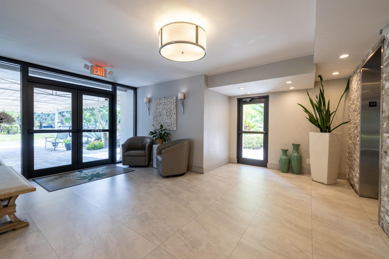 A bright lobby features tile floors, two armchairs, a large plant, and an elevator entrance — 575 Oaks Lane # 708, Pompano Beach FL 33069, POMPANO BEACH, FL