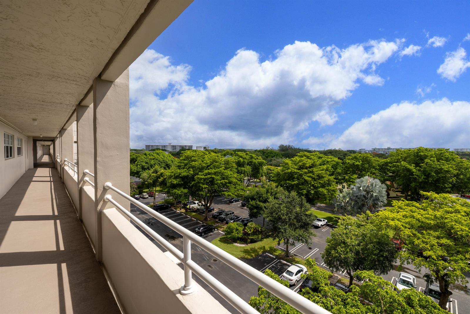 An elevated view from a covered apartment balcony overlooking a parking lot and green trees — 575 Oaks Lane # 708, Pompano Beach FL 33069, POMPANO BEACH, FL