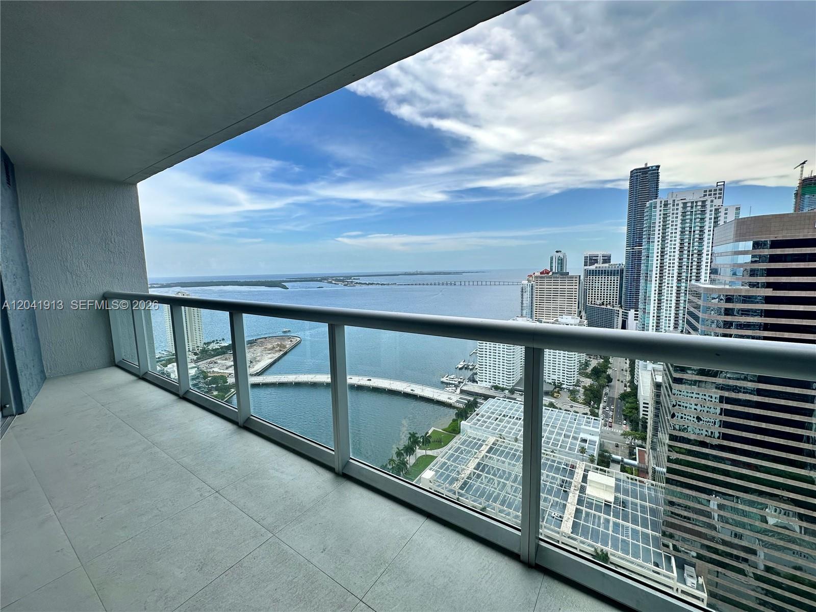 A balcony with glass railings overlooks a bay, a bridge, and a city skyline — 495 Brickell Ave # 4011, Miami FL 33131, MIAMI, FL