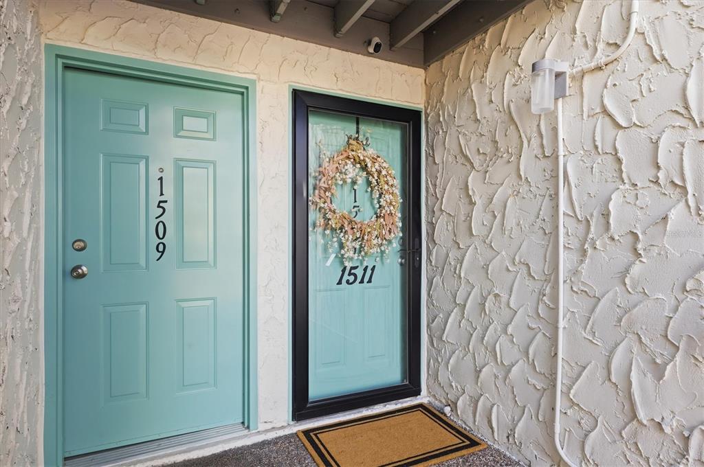 Two teal front doors with house numbers are set against a textured off-white wall — 11409 8TH STREET N UNIT 1509, ST PETERSBURG, FL