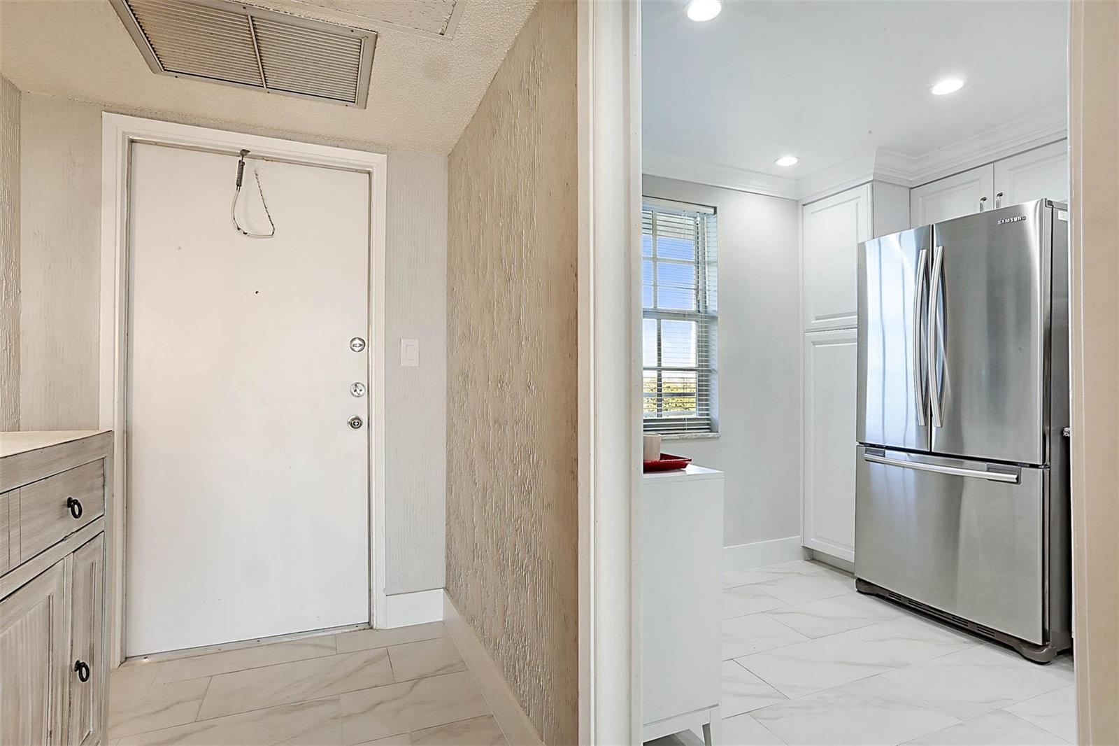 A white door opens into a hallway with a kitchen featuring a stainless steel refrigerator — 575 Oaks Lane # 703, Pompano Beach FL 33069, POMPANO BEACH, FL
