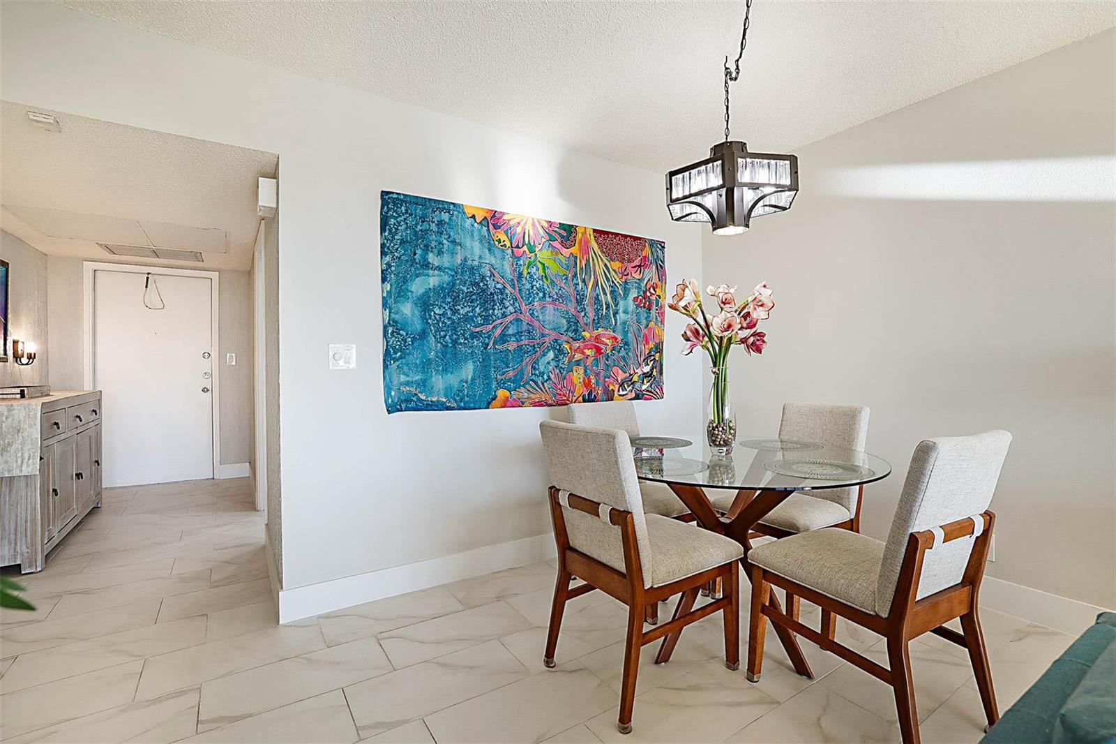A dining area features a glass-topped table, four upholstered chairs, and a colorful wall tapestry — 575 Oaks Lane # 703, Pompano Beach FL 33069, POMPANO BEACH, FL