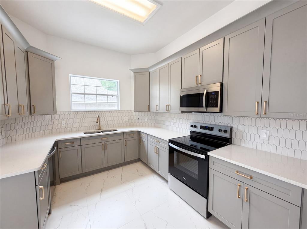 A kitchen features gray cabinets, white countertops, a white tile backsplash, and stainless steel appliances — 9405 SW 31ST LANE, GAINESVILLE, FL