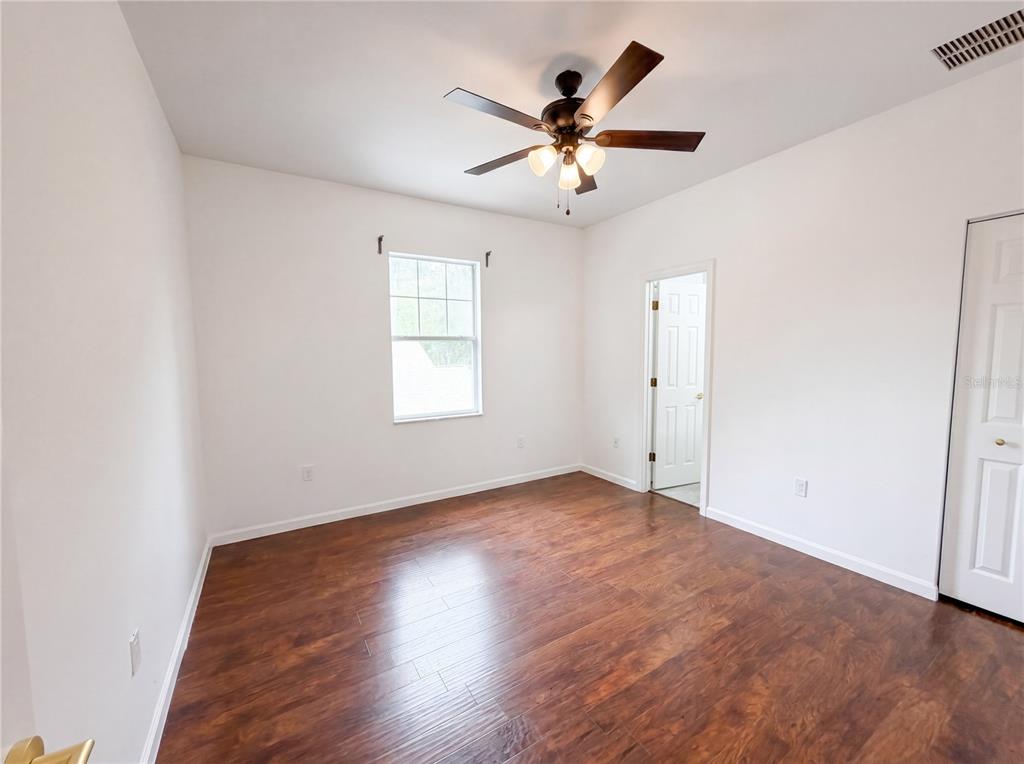 A bedroom with white walls, dark wood-look flooring, a ceiling fan, and a closet door — 9405 SW 31ST LANE, GAINESVILLE, FL