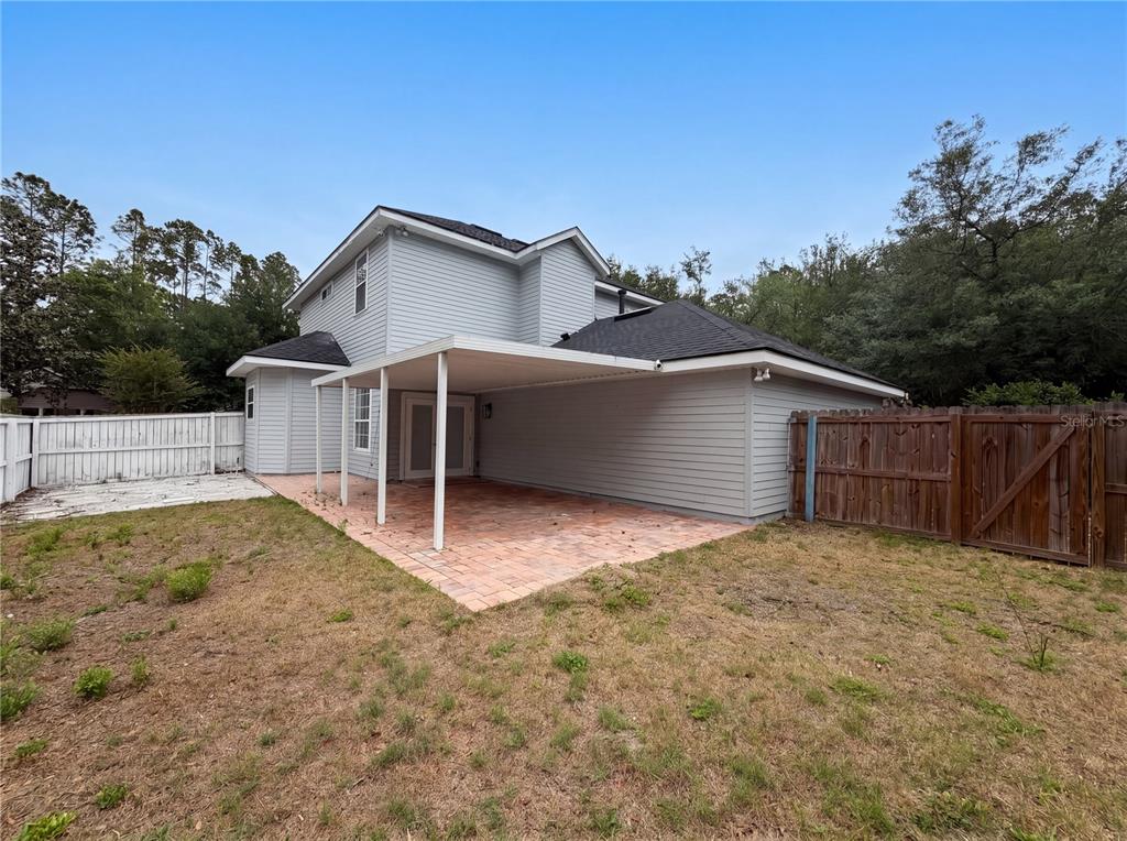 The exterior of a two-story house features a covered patio with brick pavers and fencing — 9405 SW 31ST LANE, GAINESVILLE, FL