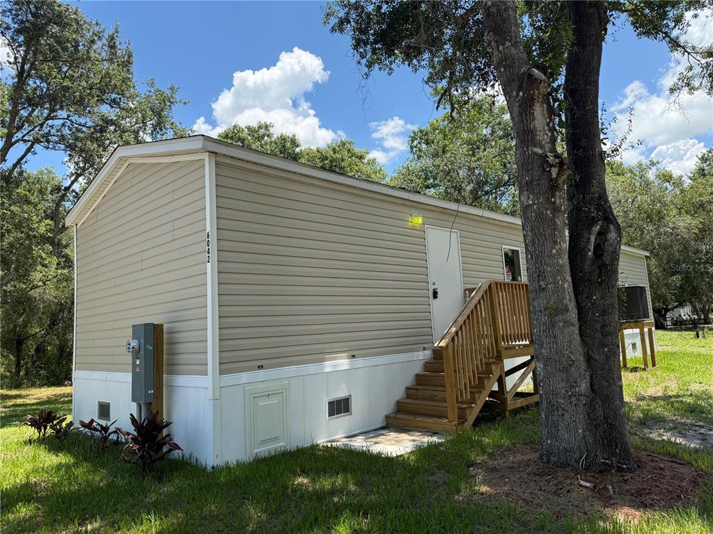 A tan mobile home with a wooden staircase leading to a white entry door — 6042 SW MIAMI AVENUE, ARCADIA, FL