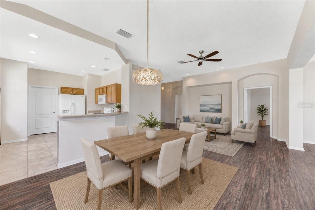 An open-concept dining area with a wooden table leads into a living room with furniture — 1149 EMERALD DUNES DRIVE, SUN CITY CENTER, FL