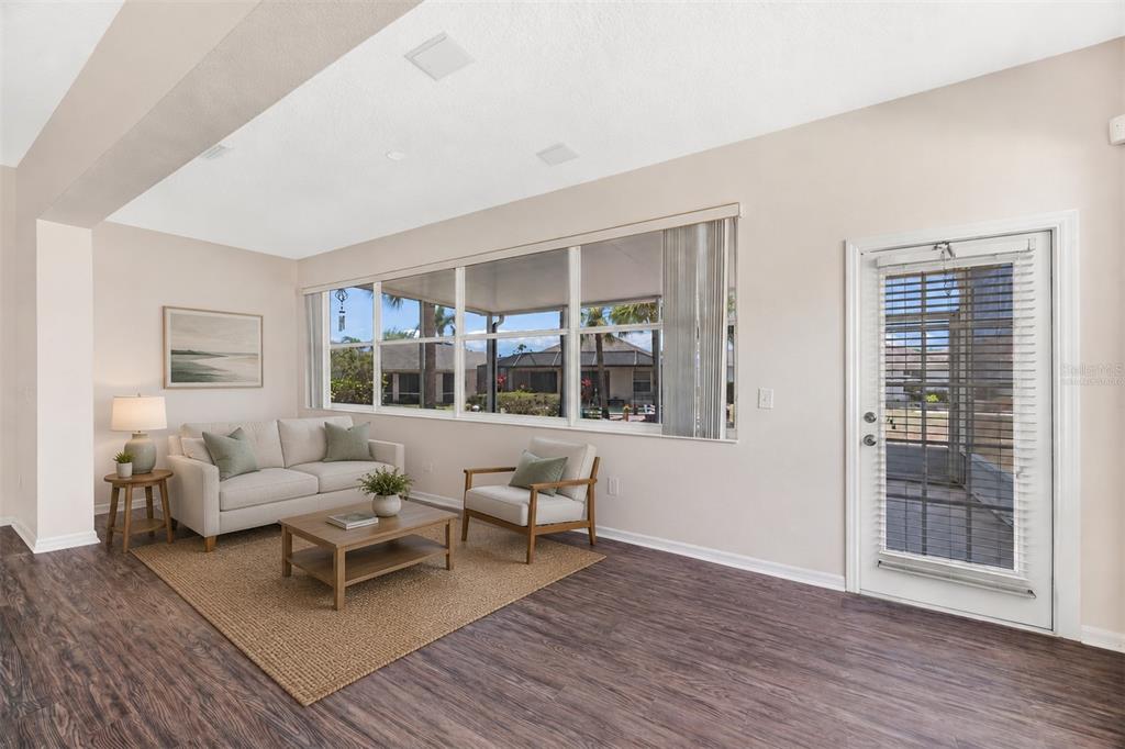 A living room with wood-look flooring, a sofa, an armchair, and a glass-paned exterior door — 1149 EMERALD DUNES DRIVE, SUN CITY CENTER, FL