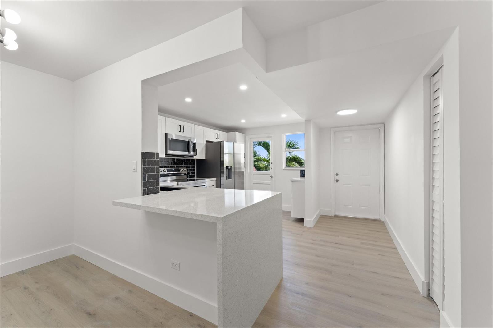 A kitchen with white cabinets, a quartz breakfast bar, and light wood-look flooring — 441 NE 195th Street # 302, Miami FL 33179, MIAMI, FL