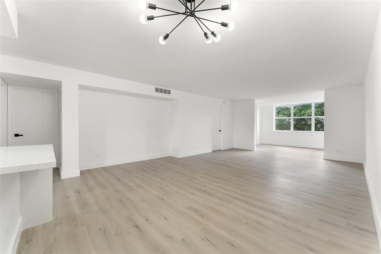 An empty living room features white walls, light wood-look flooring, and a modern sputnik chandelier — 441 NE 195th Street # 302, Miami FL 33179, MIAMI, FL