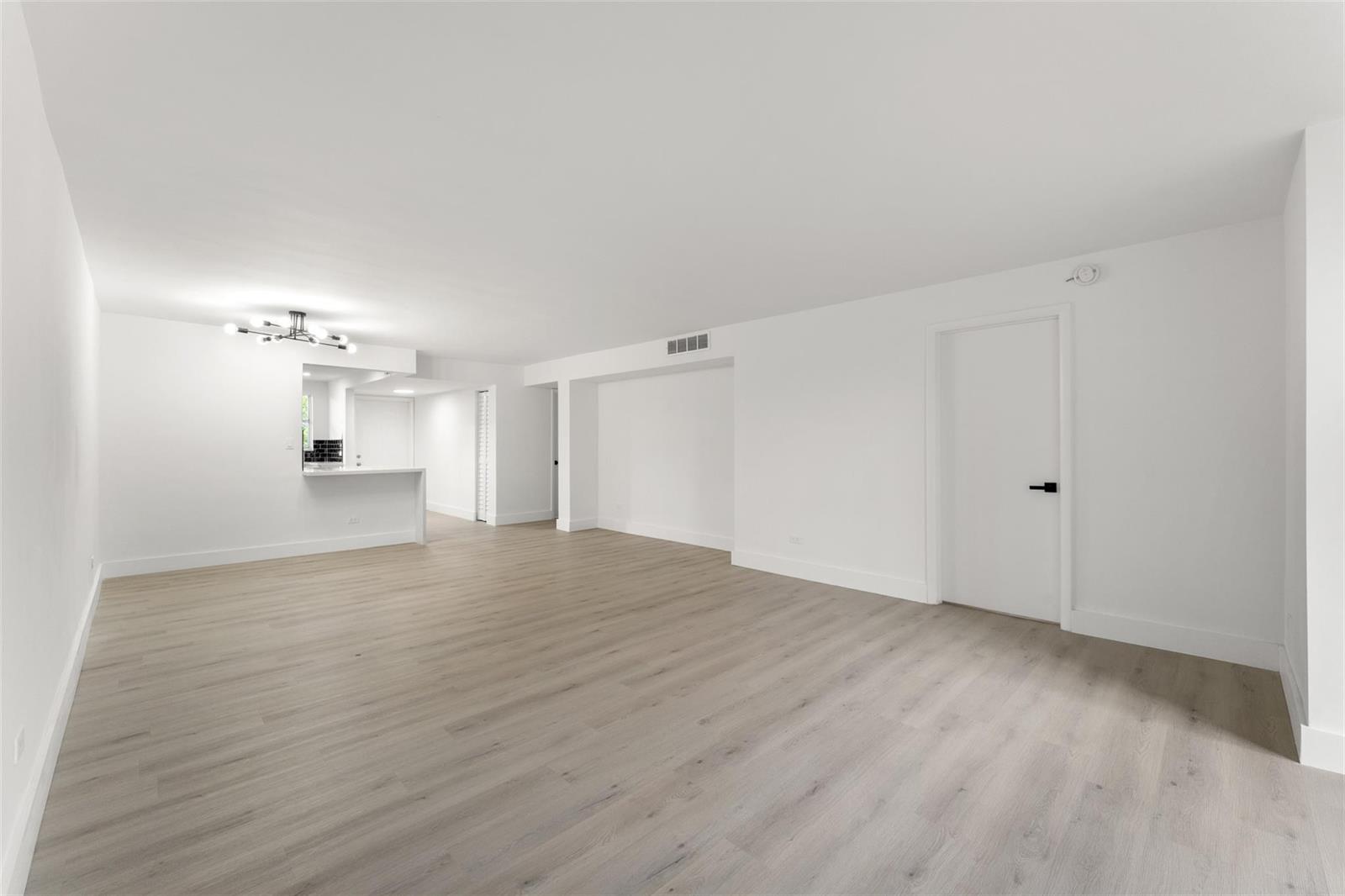 An empty living room features light wood-look flooring, white walls, and a small kitchen pass-through — 441 NE 195th Street # 302, Miami FL 33179, MIAMI, FL