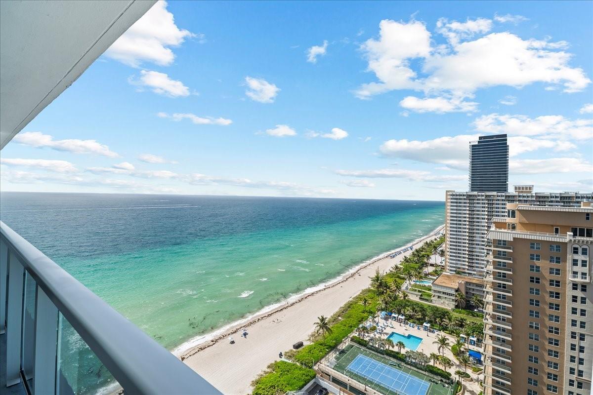 A high-angle view from a balcony overlooking a beach, ocean, and nearby high-rise buildings — 1890 S Ocean Drive, Hallandale Beach FL 33009, HALLANDALE BEACH, FL