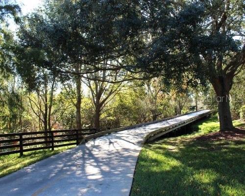 A paved path leads to a wooden bridge surrounded by trees and a wooden fence — 1709 SONORA STREET, THE VILLAGES, FL