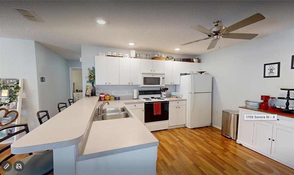 A kitchen features white cabinets, a breakfast bar, stainless steel appliances, and wood-look flooring — 1709 SONORA STREET, THE VILLAGES, FL