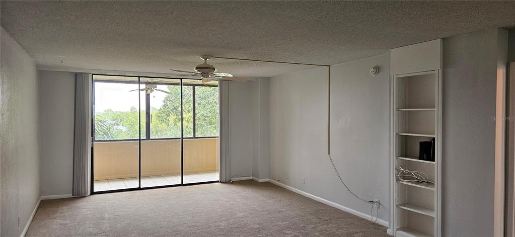 A living room features beige carpeting, a ceiling fan, sliding glass doors, and built-in shelving — 2617 COVE CAY DRIVE UNIT 311, CLEARWATER, FL