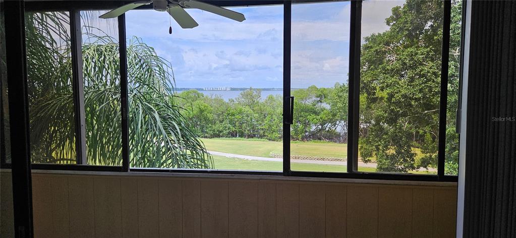 A view of a grassy lawn and water through a screened-in porch with sliding windows — 2617 COVE CAY DRIVE UNIT 311, CLEARWATER, FL