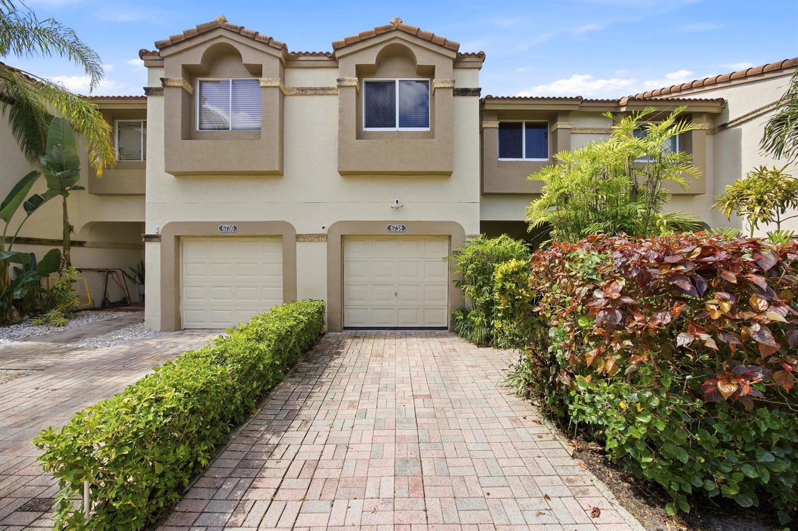 A two-story townhouse exterior features two beige garage doors and a brick paver driveway — 6738 Via Regina, Boca Raton FL 33433, BOCA RATON, FL