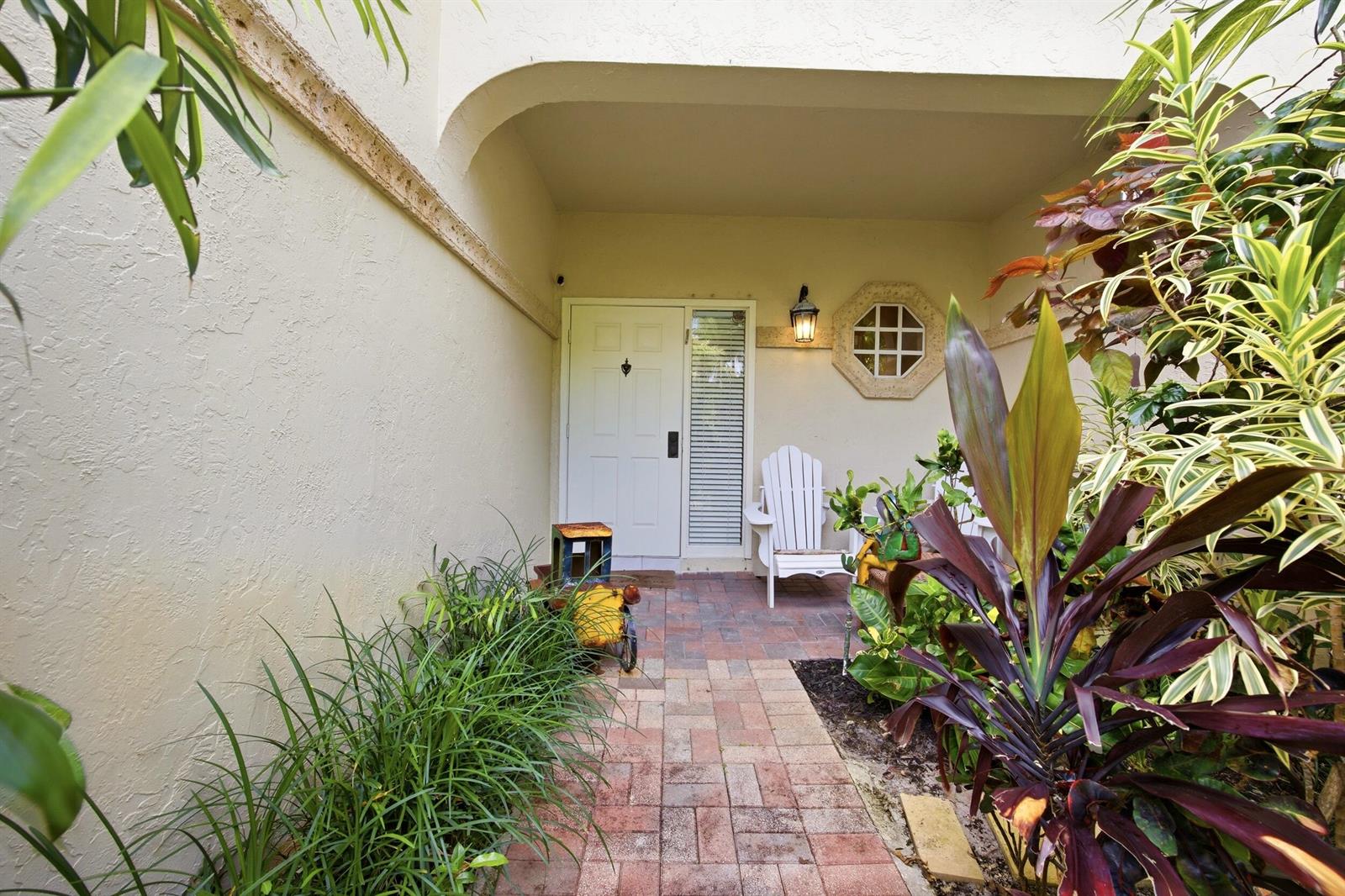 A brick walkway leads to a white front door with a side window and chair — 6738 Via Regina, Boca Raton FL 33433, BOCA RATON, FL