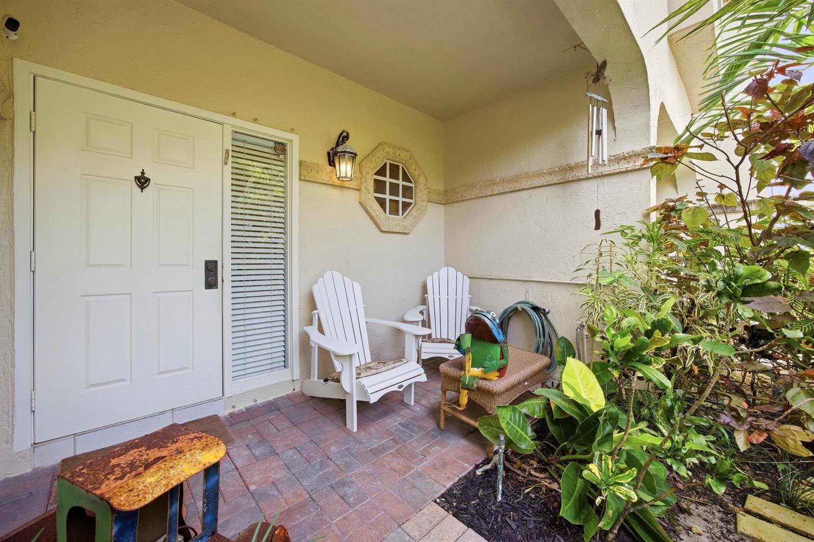 A white front door opens onto a brick patio with two white Adirondack chairs — 6738 Via Regina, Boca Raton FL 33433, BOCA RATON, FL