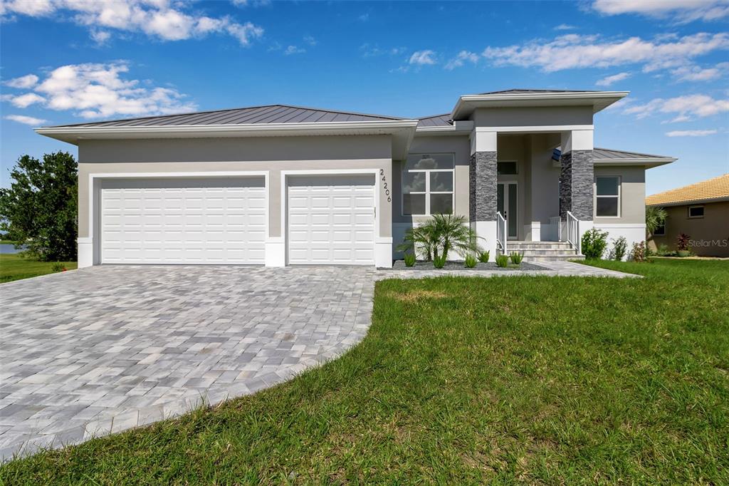 A modern single-story house with a paver driveway, two-car garage, and stone-accented entryway — 24206 SANTA INEZ ROAD, PUNTA GORDA, FL
