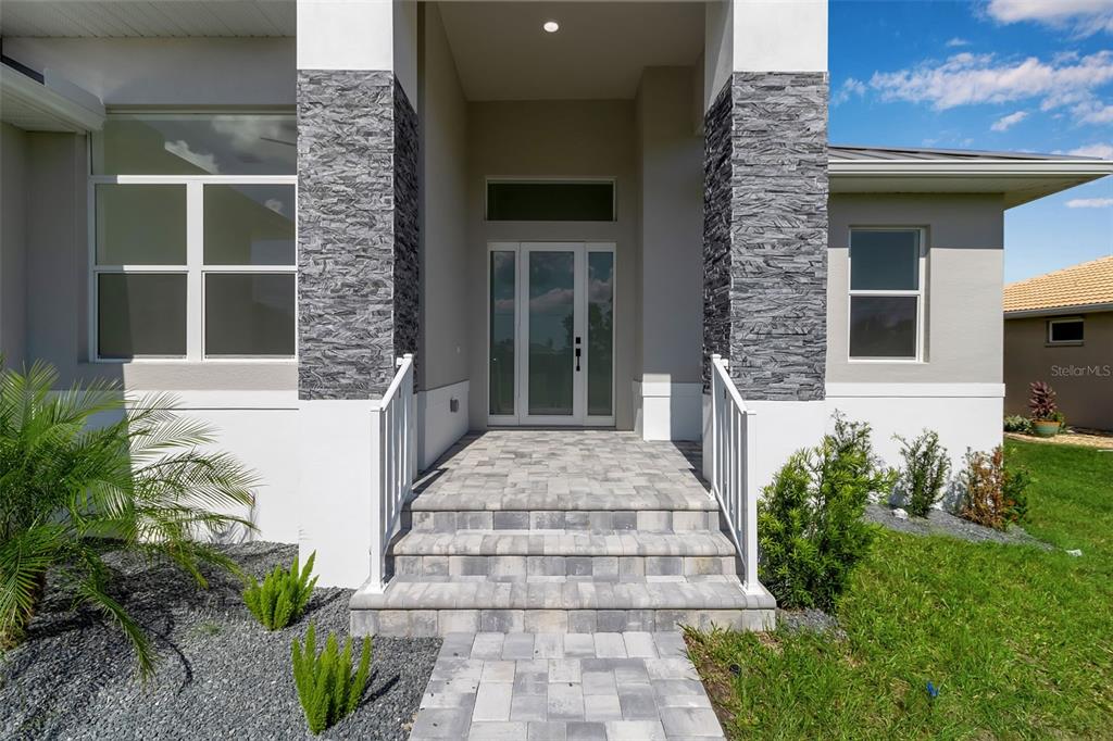 The front entrance of a house features a stone-tiled porch, gray stone pillars, and a glass door — 24206 SANTA INEZ ROAD, PUNTA GORDA, FL