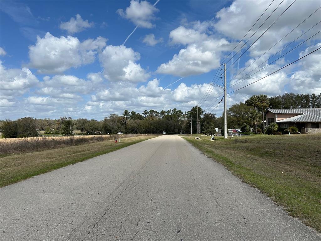 A paved road leads toward a line of trees under a bright, cloudy sky — NW 104TH TERRACE, ALACHUA, FL
