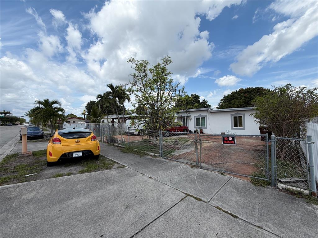A yellow car is parked on the grass in front of a fenced residential property — 445 E 43RD STREET, HIALEAH, FL