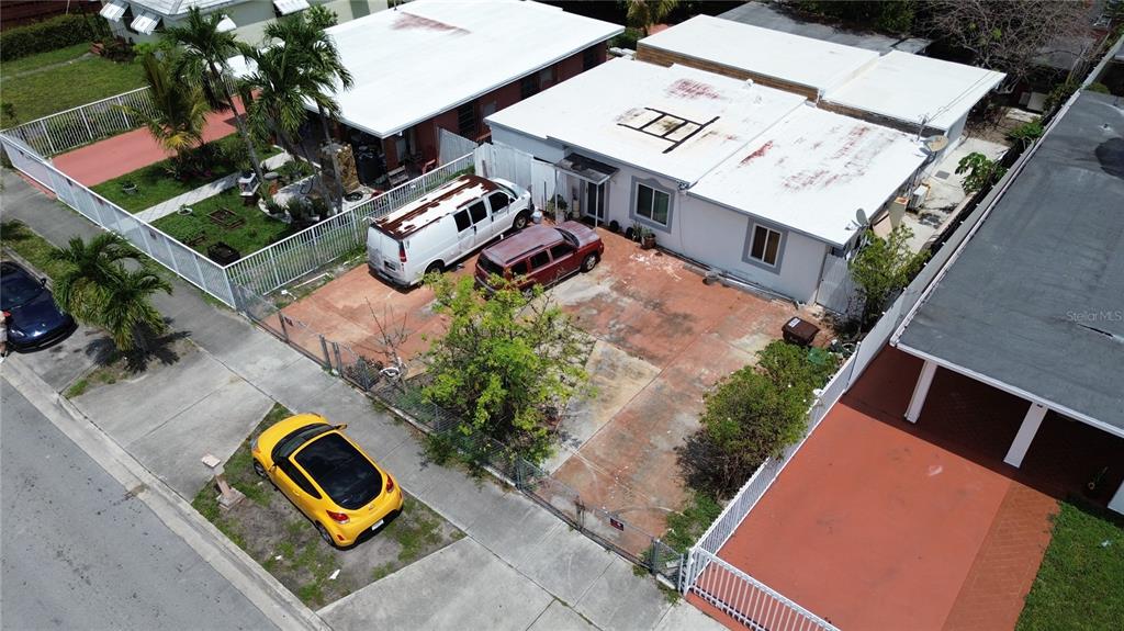 An aerial view shows a white house with a large paved driveway and fenced yard — 445 E 43RD STREET, HIALEAH, FL