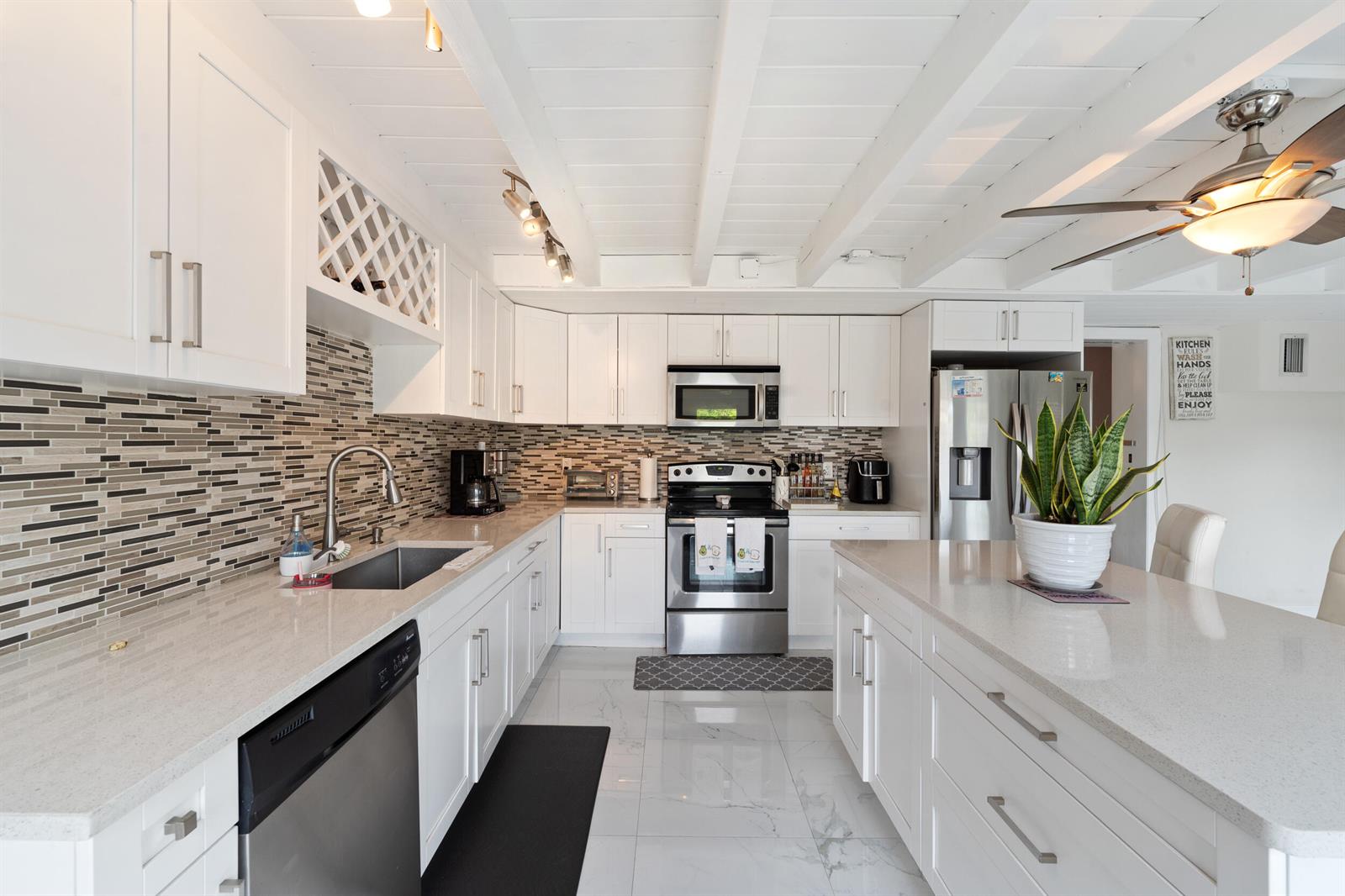 A bright kitchen features white cabinets, quartz countertops, stainless steel appliances, and a ceiling fan — 808 Wright Drive, Lake Worth FL 33461, LAKE WORTH, FL