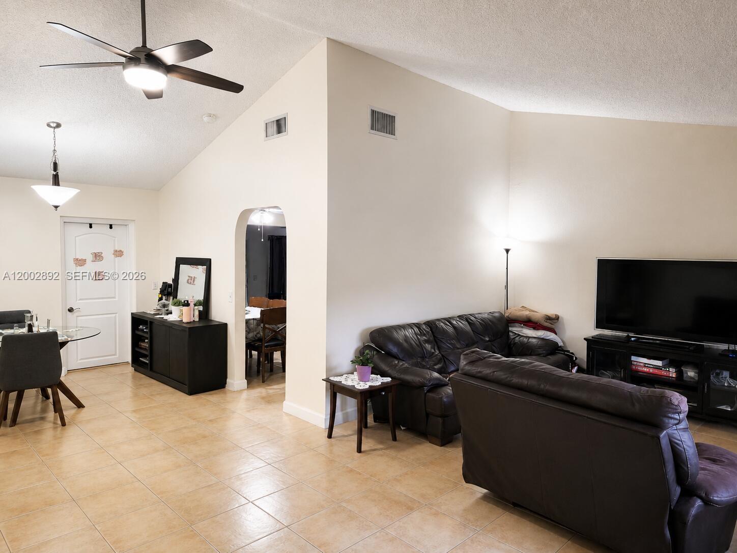 A living room and dining area feature vaulted ceilings, tile floors, and dark leather furniture — 12011 NW 33rd St, Sunrise FL 33323, SUNRISE, FL