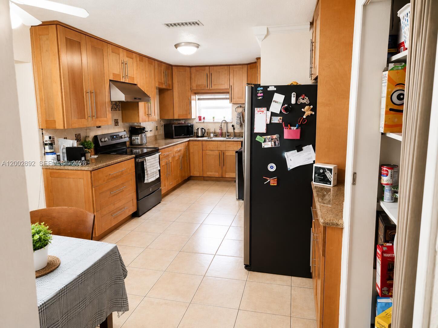 A kitchen features light wood cabinets, black appliances, tile flooring, and a pantry — 12011 NW 33rd St, Sunrise FL 33323, SUNRISE, FL