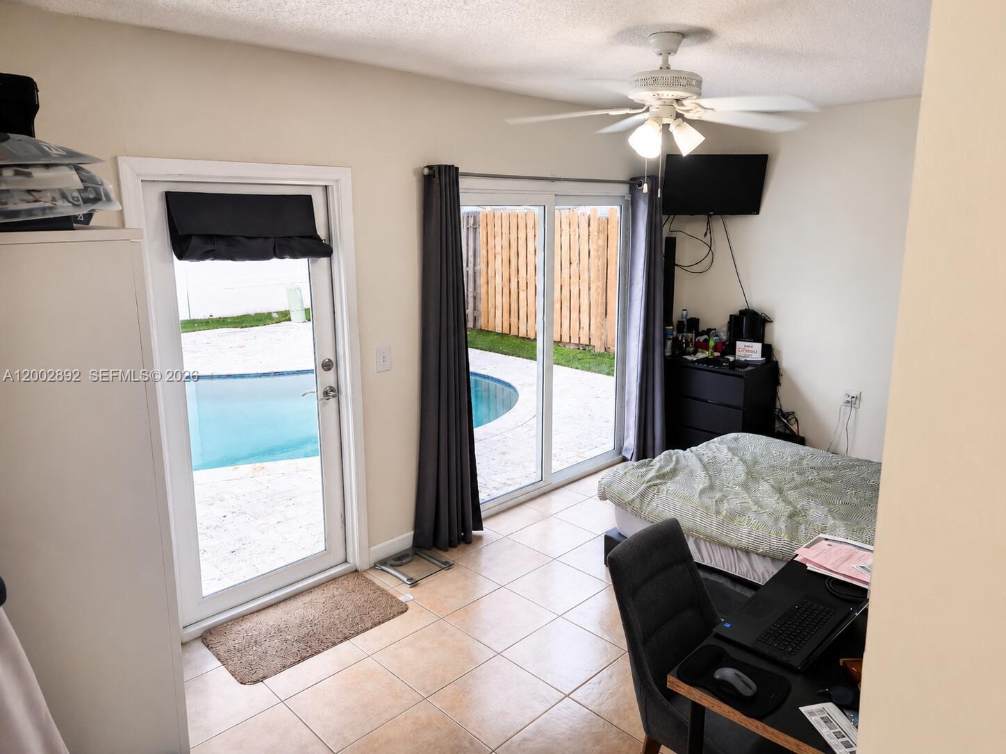 A bedroom with tile flooring, a ceiling fan, a bed, a desk, and sliding glass doors — 12011 NW 33rd St, Sunrise FL 33323, SUNRISE, FL