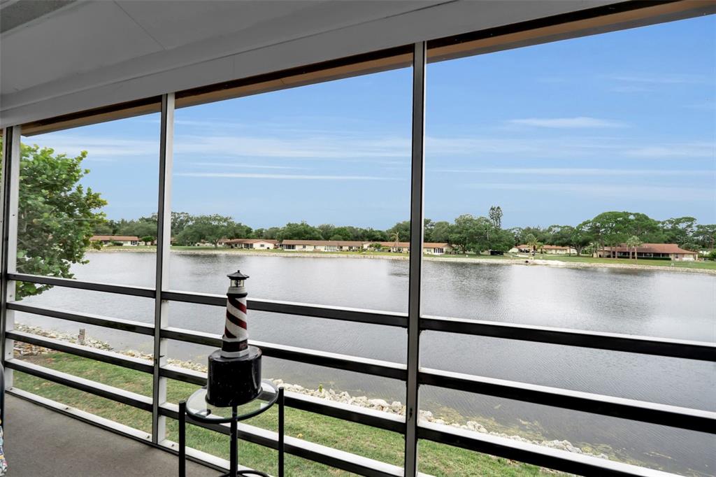 A screened-in porch overlooks a lake with a small decorative lighthouse on a side table — 4470 NARRAGANSET TRAIL UNIT 90A, SARASOTA, FL