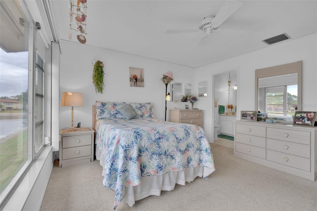 A bedroom features a bed with a tropical print comforter, light-colored furniture, and a window view — 4470 NARRAGANSET TRAIL UNIT 90A, SARASOTA, FL