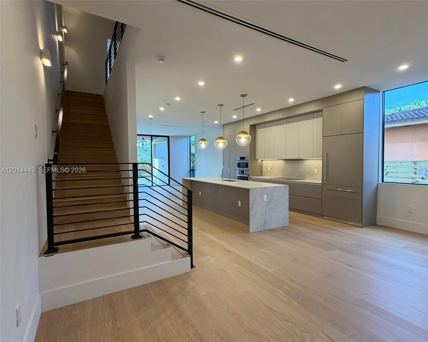 A modern kitchen with a stone island and wood flooring sits beside a staircase — 1501 SW 21st St, Miami FL 33145, MIAMI, FL