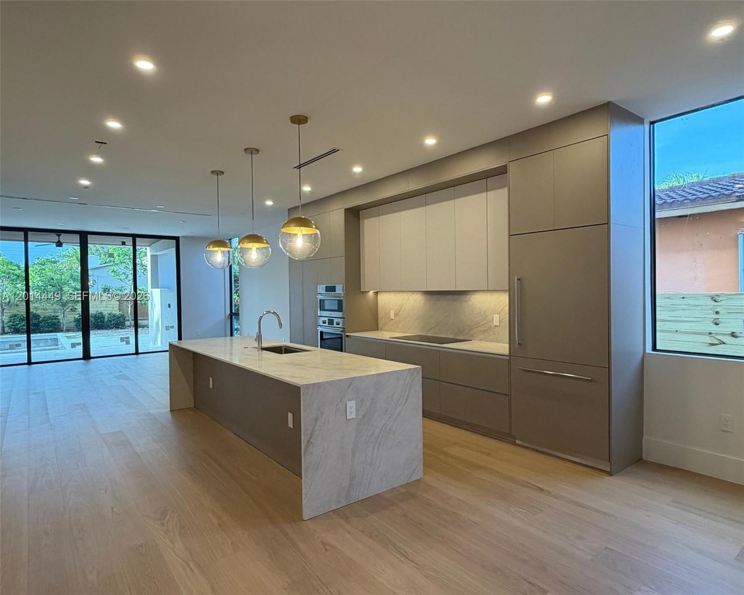 A modern kitchen features a marble-topped island, light wood flooring, and integrated cabinetry — 1501 SW 21st St, Miami FL 33145, MIAMI, FL