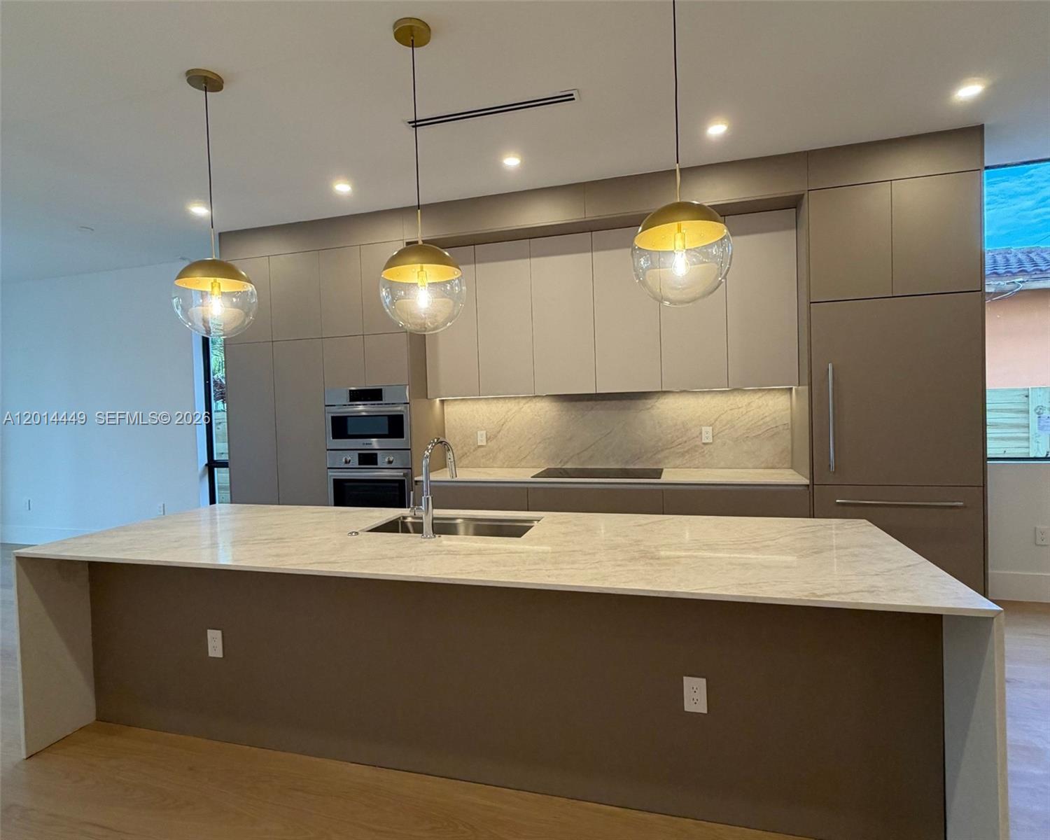 A modern kitchen features a large marble-topped island, taupe cabinetry, and three gold pendant lights — 1501 SW 21st St, Miami FL 33145, MIAMI, FL