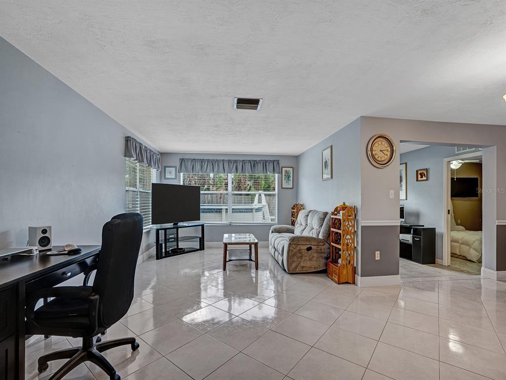 A living room features light-colored tile flooring, a desk, a sofa, and a television — 6732 WILLIAM TELL DRIVE, NEW PORT RICHEY, FL