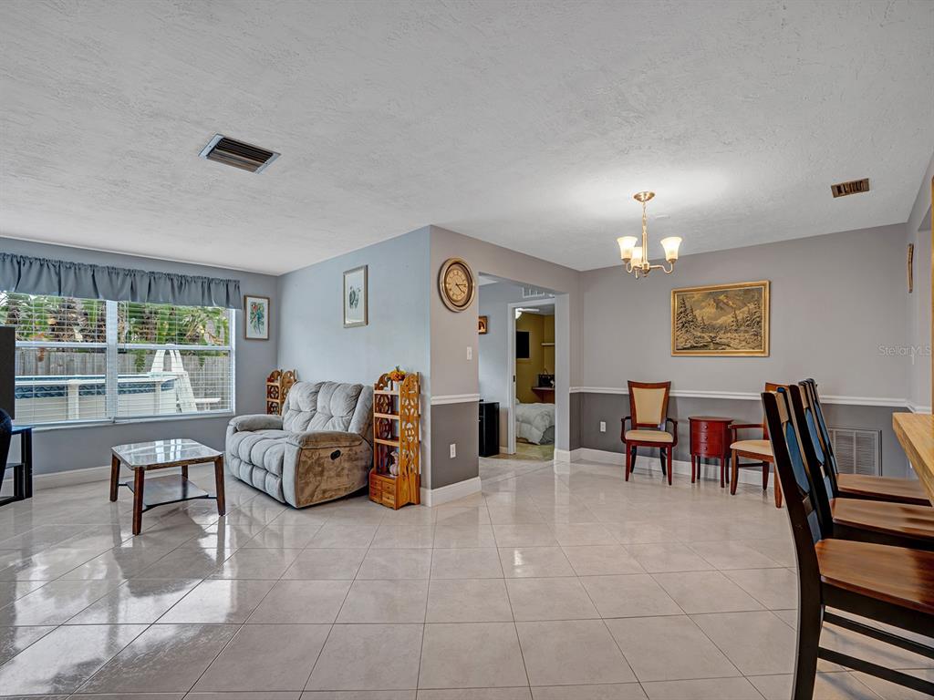 A living and dining area with light tile floors, gray walls, and a view of a pool — 6732 WILLIAM TELL DRIVE, NEW PORT RICHEY, FL